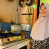 Person smiling, using biogas cookstove to prepare doughnuts they sell locally