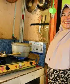 Person smiling, using biogas cookstove to prepare doughnuts they sell locally