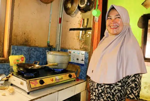 Person smiling, using biogas cookstove to prepare doughnuts they sell locally